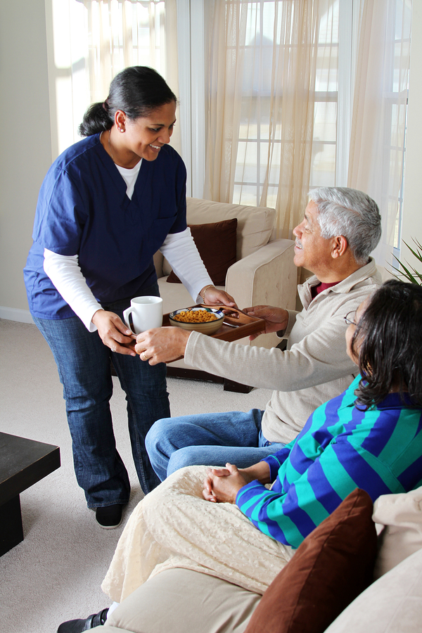 Caregiver serving a warm meal and drink to a couple at home