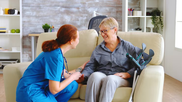 Caregiver sitting with a smiling older adult in her living room chair