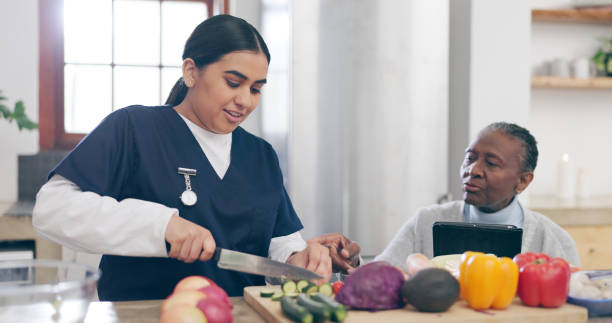 Caregiver chopping fresh vegetables while an older woman sits at the kitchen counter