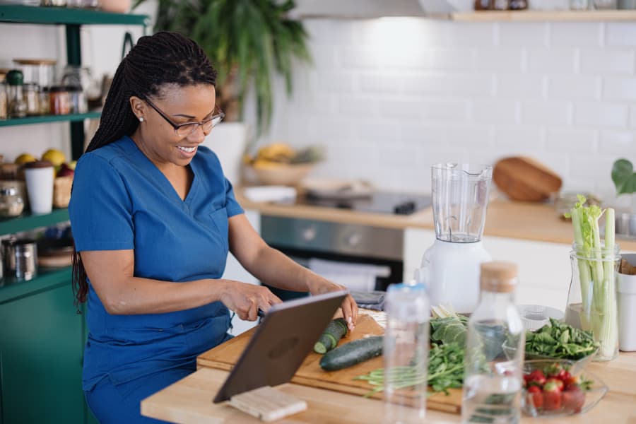 Caregiver preparing fresh produce in a kitchen while checking a tablet