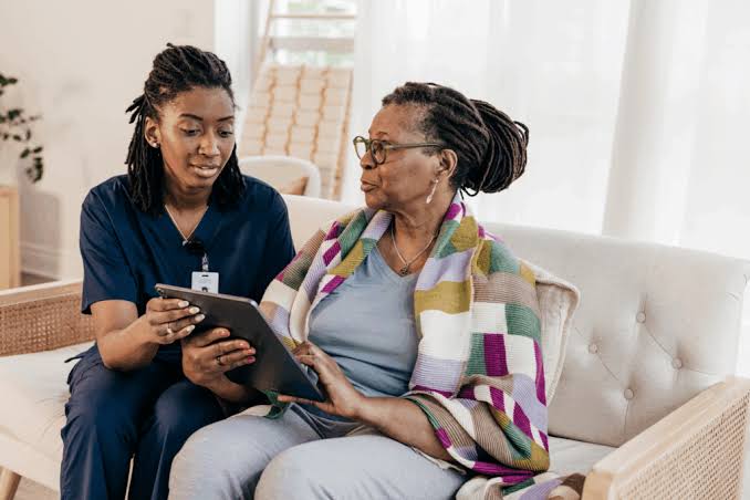 Caregiver sitting on a sofa looking at a tablet with an older woman