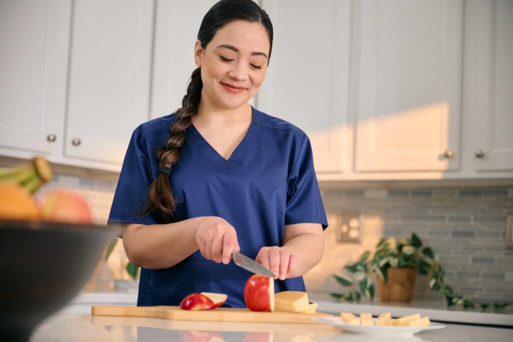 Caregiver in navy scrubs tidying and slicing fruit at a clean kitchen counter